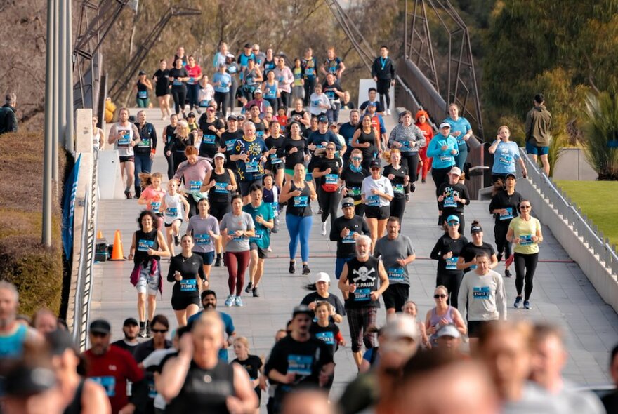 A large group of people running over a bridge during a fun run. 