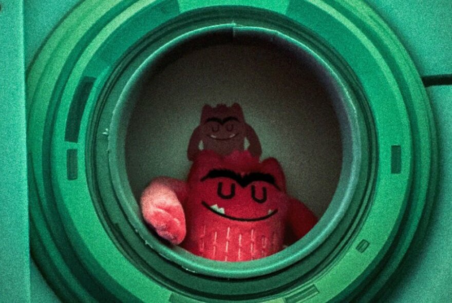A red plushie toy sitting inside a hollowed wall cavity.