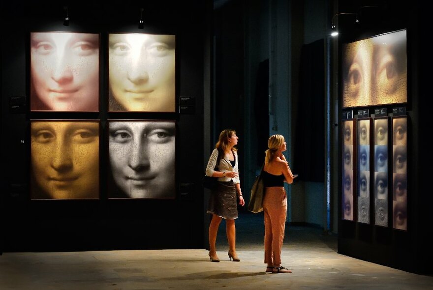 Two women in a dark room with projections of the Mona Lisa. 
