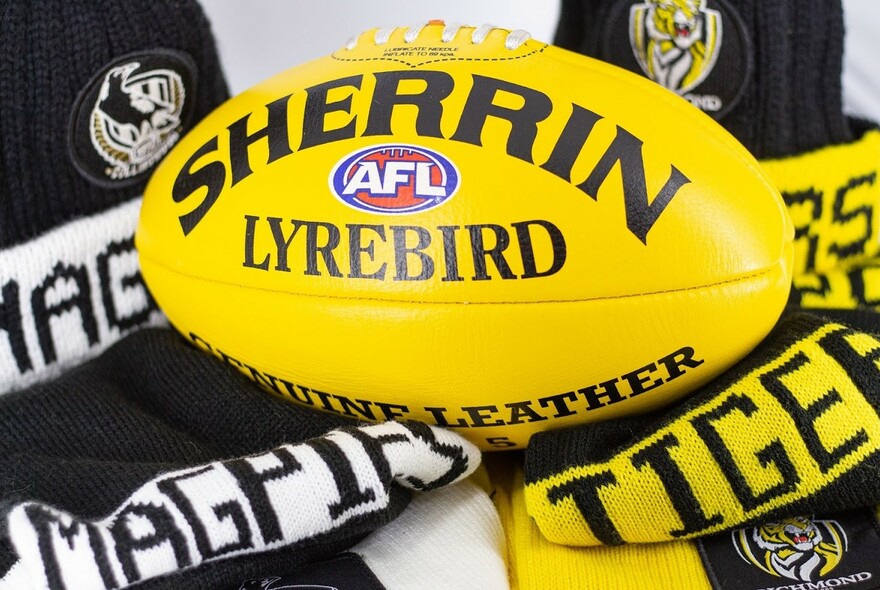 Yellow Sherrin branded AFL football resting on two AFL club scarves.
