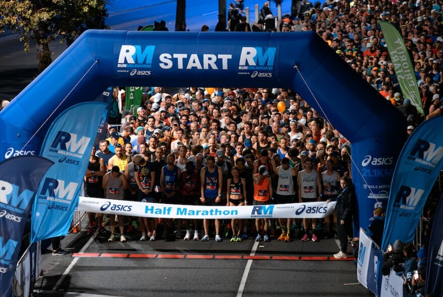 A marathon start line with many people in bibs lined up ready to start a race under a large blue inflatable archway.