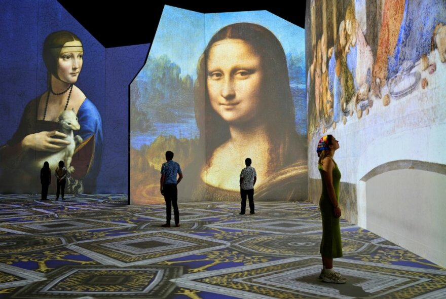 People in a very large space with Leonardo da Vinci artwork projected on the walls.