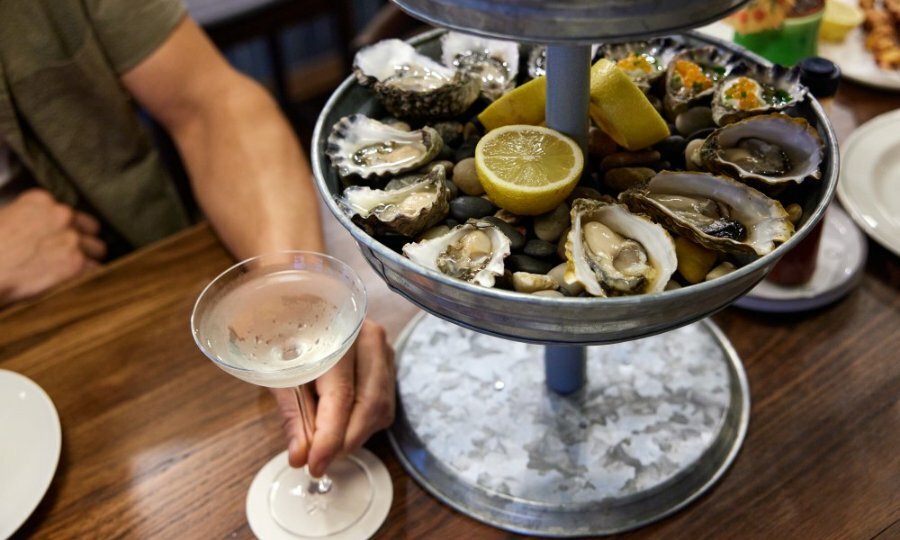 Someone holding a glass of wine next to a tiered silver tray of oysters.