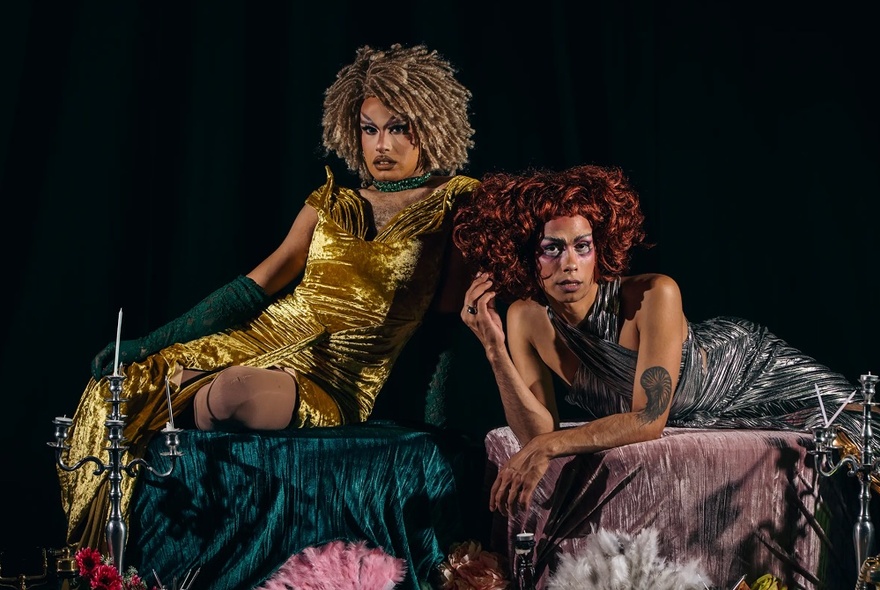 Two drag queens in renaissance inspired dresses lounging and staring blankly.