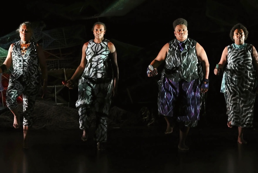 Four dancers in similar outfits on a darkened stage performing. 