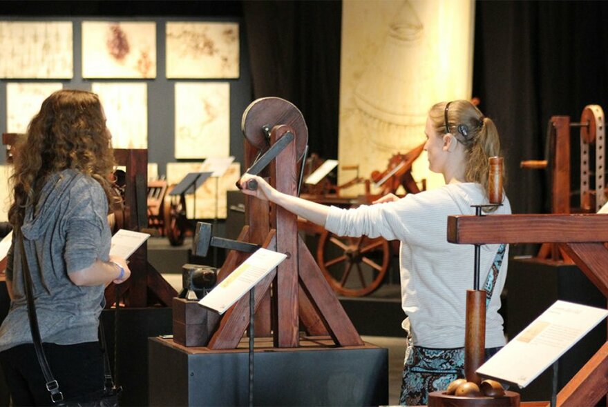 Two women at a hands-on exhibit trying out a replica of one of Leonardo da Vinci's machines.