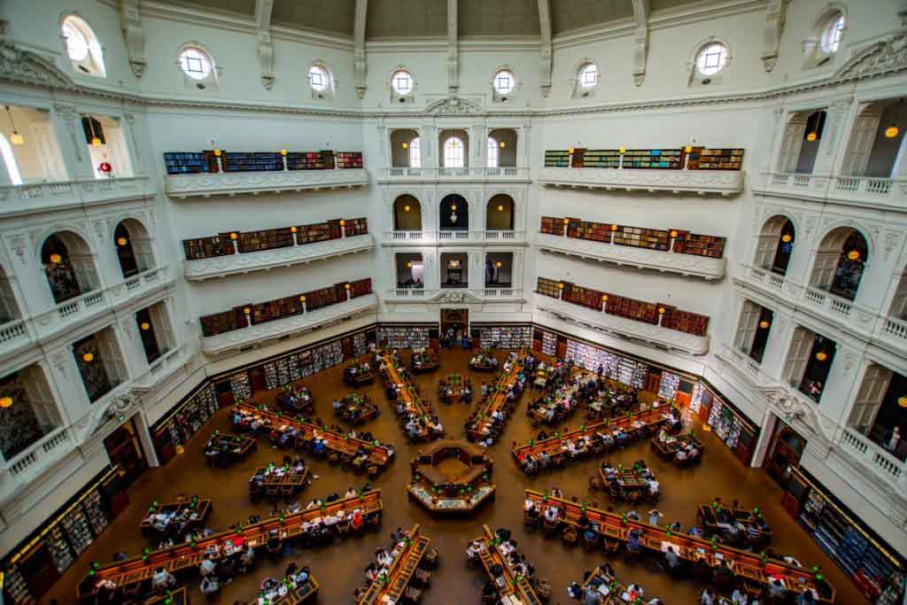 A huge old fashioned room with people reading at rows of desks on the ground floor
