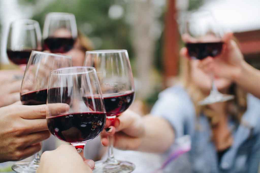 People holding up glasses of red wine and clinking them together
