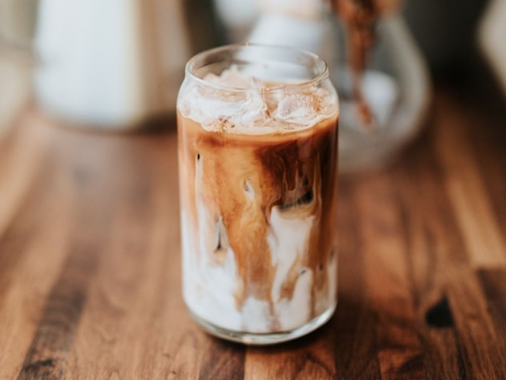 An iced coffee in a clear glass on a wooden bench