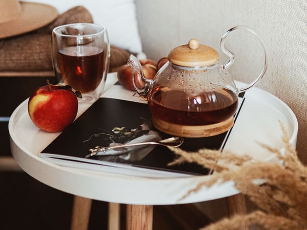 A tea pot on a small table with mugs and magazines beside it