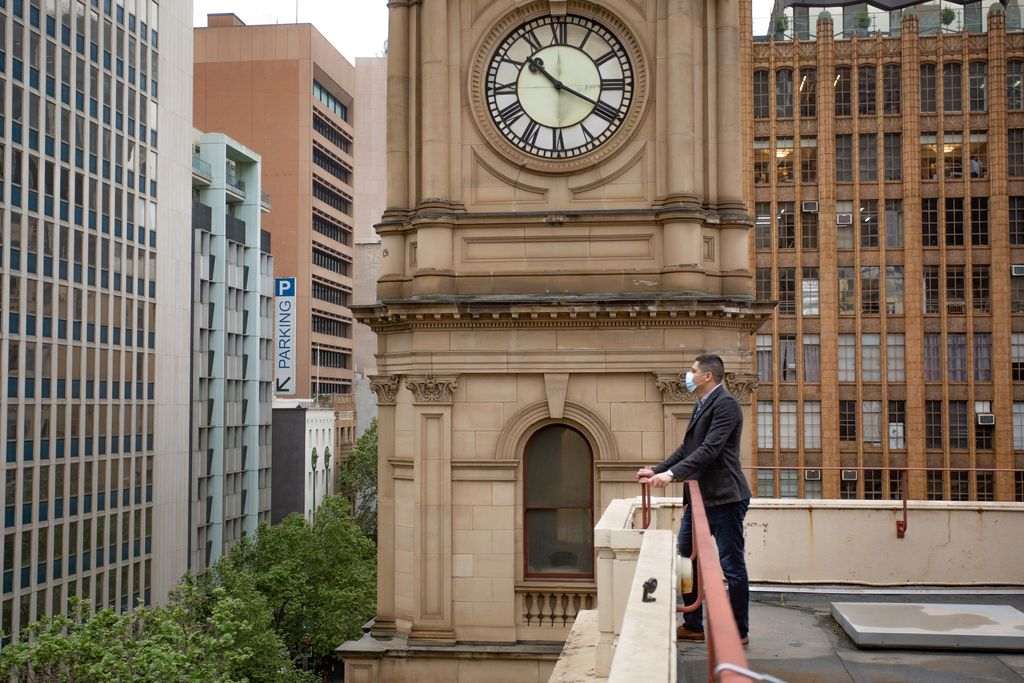 A man on a balcony with a large clocktower behind him